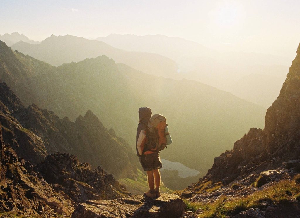 Man standing on a mountain top looking out with his rucksack, this is on the book a call page and shows that as long as you have a phone you can travel and work from anywhere 